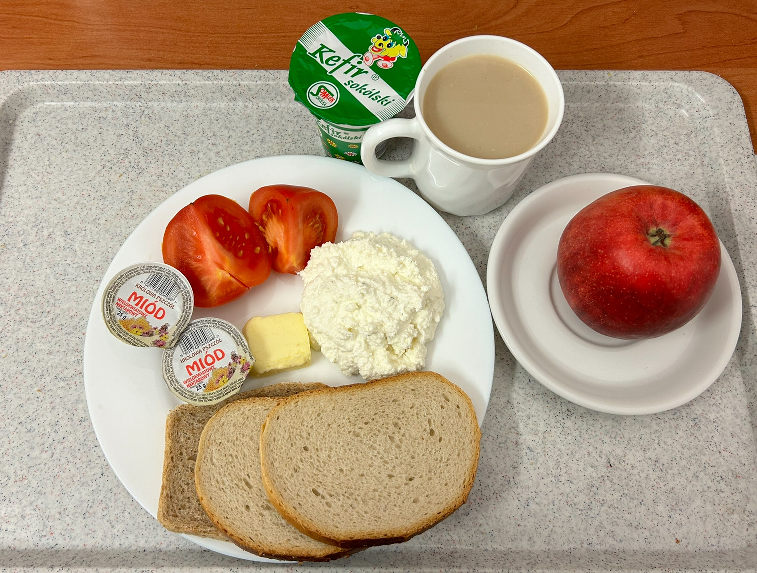 Na zdjęciu znajduje się: Kefir, Kawa zbożowa z mlekiem, Chleb mieszany pszenno-żytni, Chleb Graham, Masło extra 82%, Miód, Twarożek, Jabłko, Pomidor